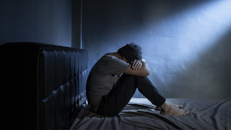 Man sitting on bed with head down in dimly lit room