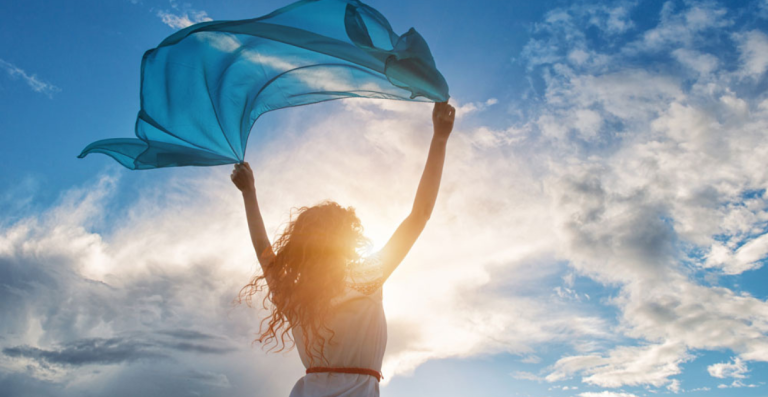 Woman outdoors holding fabric in sunlight against blue sky