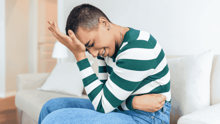 Woman holding her lower abdomen while sitting on bed