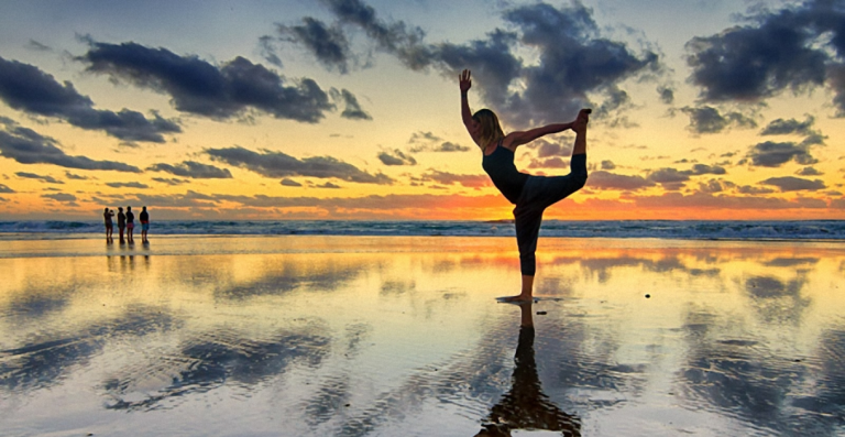Person practicing yoga on beach at sunset