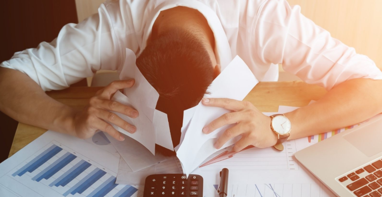 Man sitting at desk with head down over paperwork showing stress