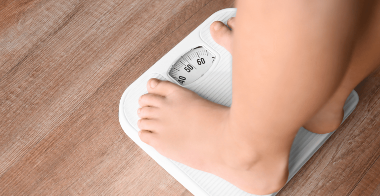 Person standing on a weighing scale representing weight gain