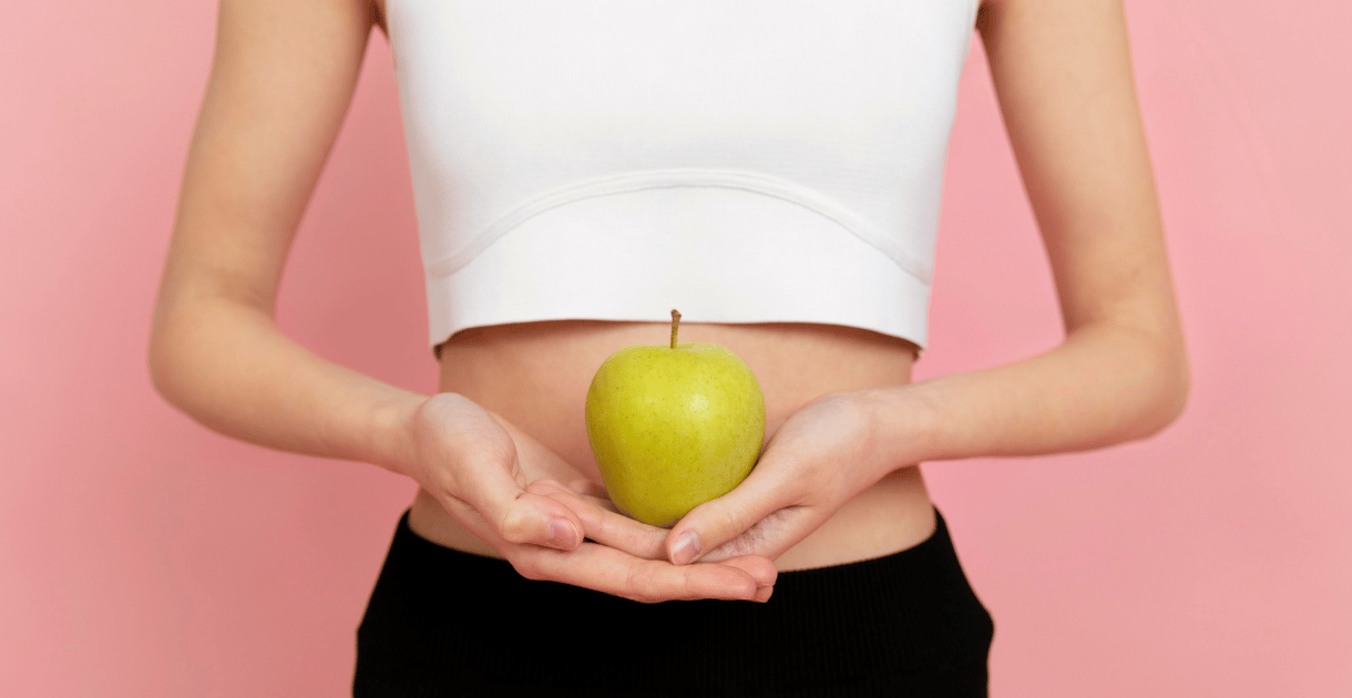Woman holding green apple in front of stomach representing gut health